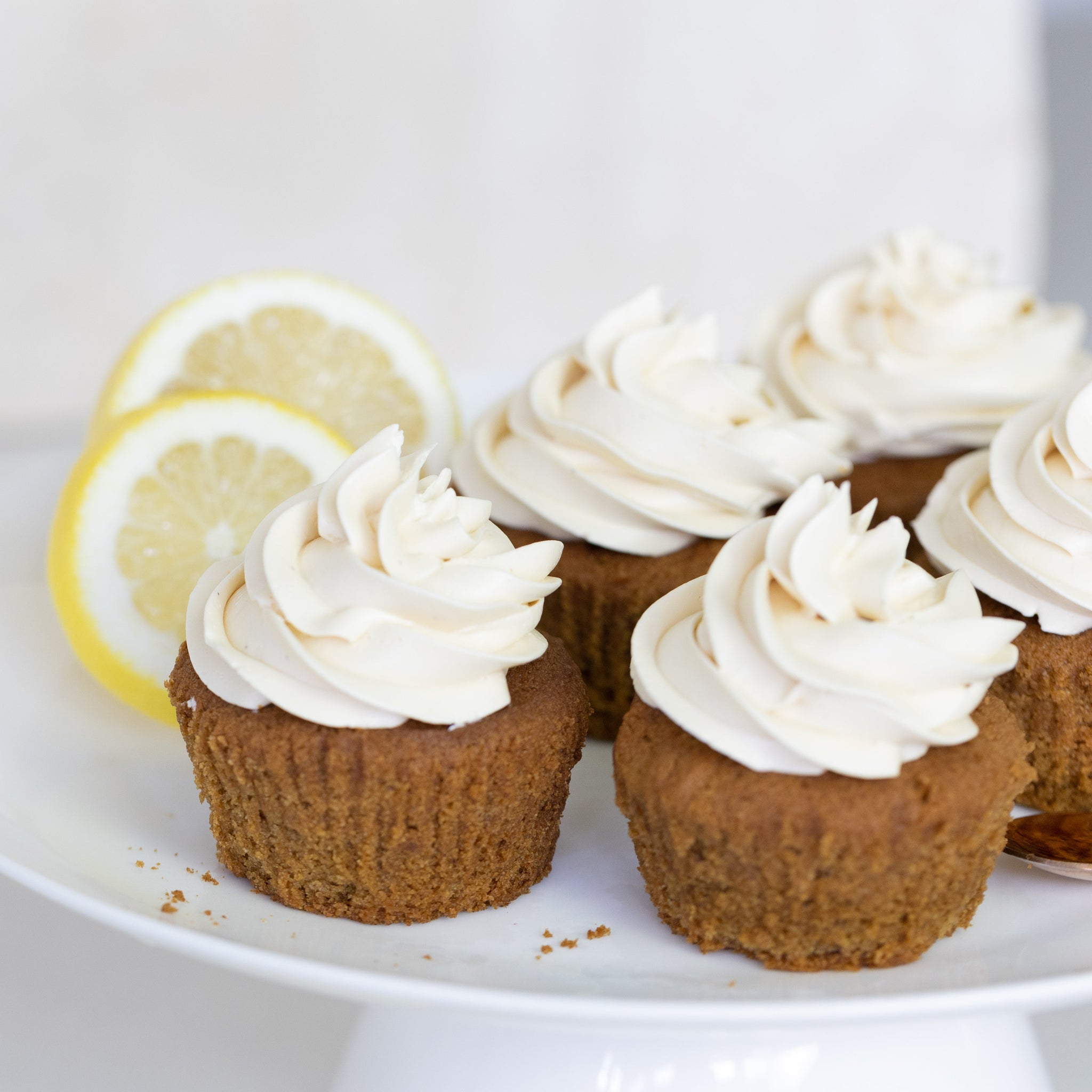 Cupcakes with lemon frosting on a white plate with lemon slices.