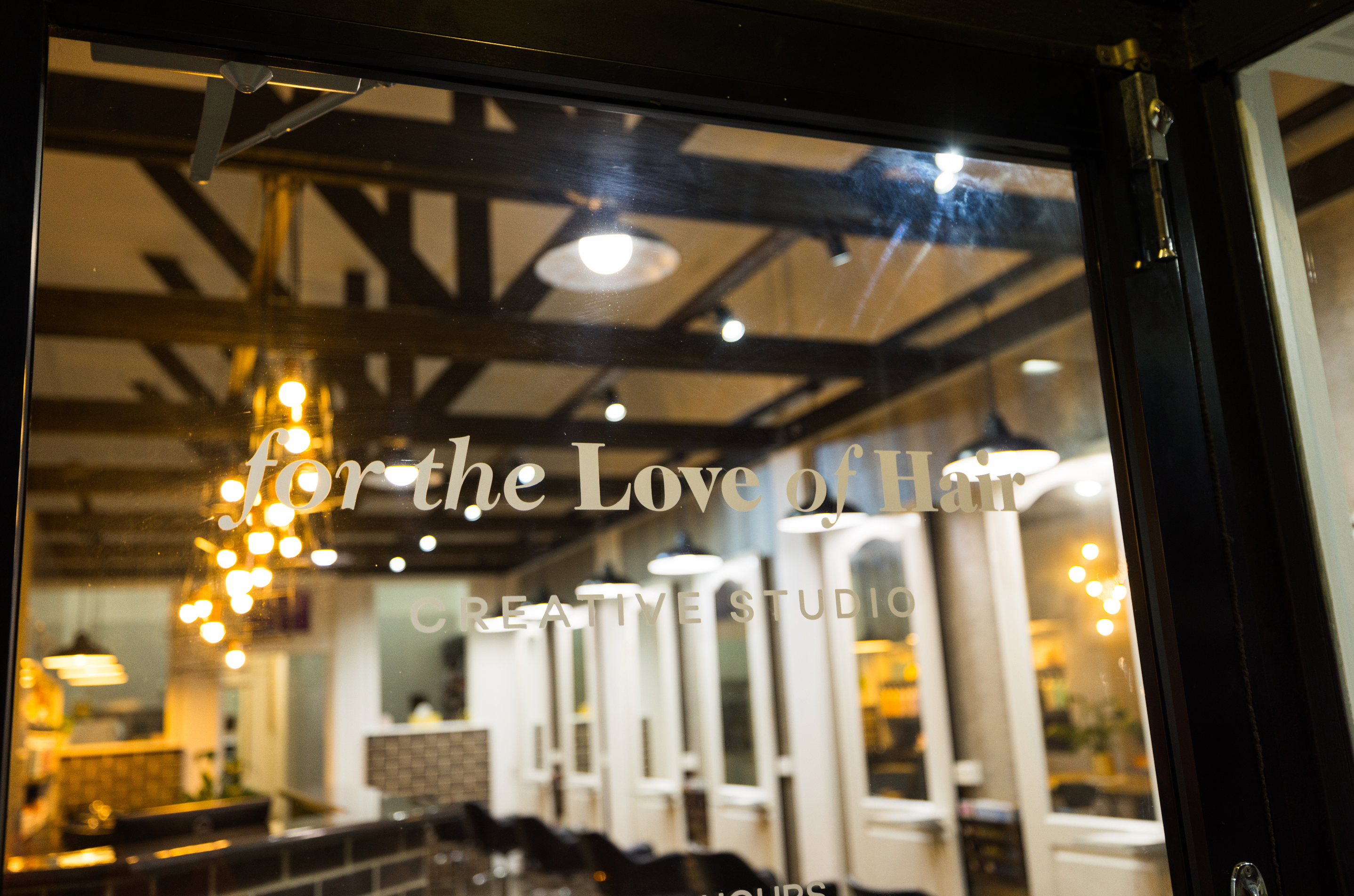 Glass door with 'For the Love of Hair' Hairdressers Mackay text, reflecting interior decor.