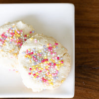 Two cookies with colorful sprinkles on a white plate against a wooden background